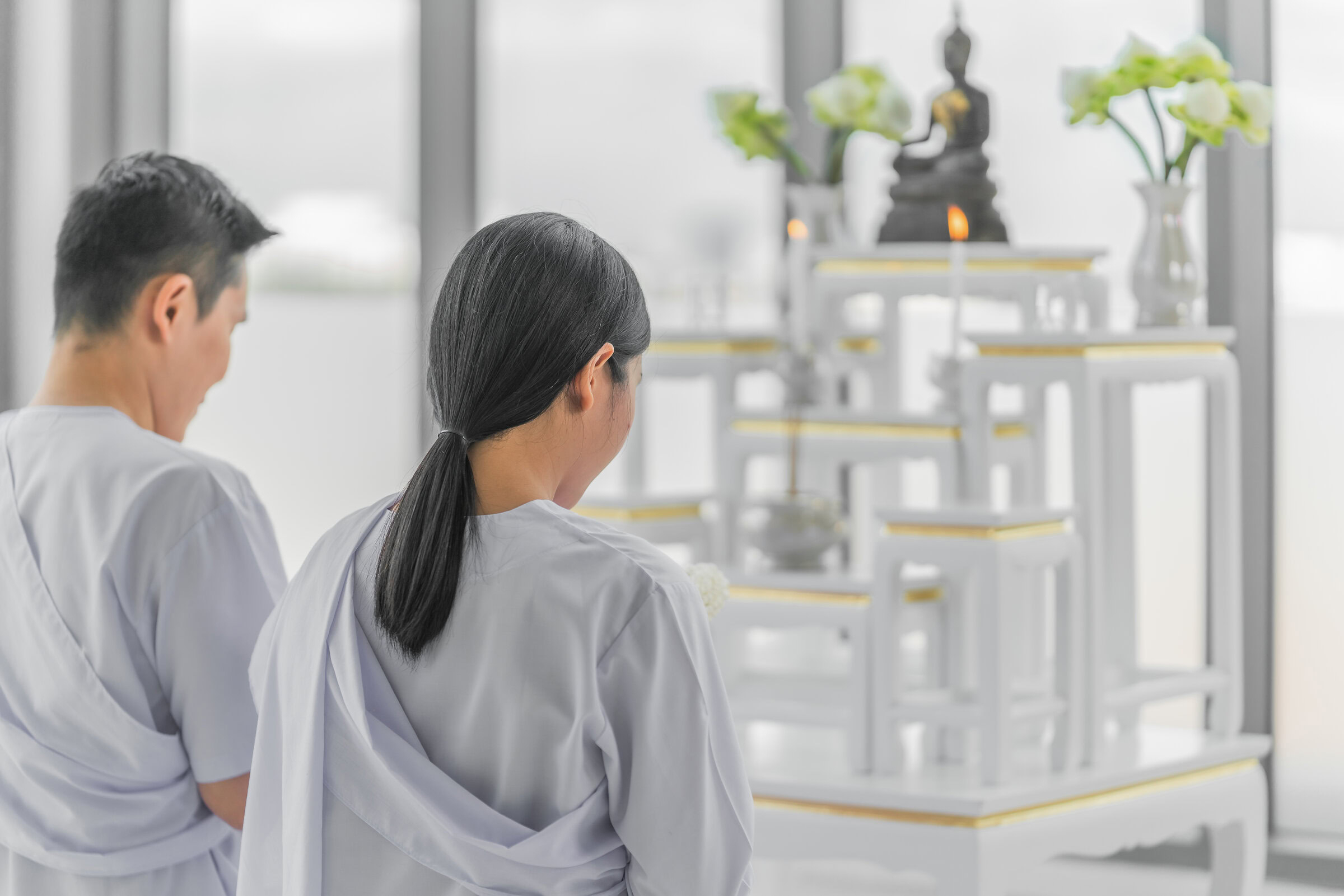 สามีภรรยากำลังจุดธูปไหว้พระและทำสมาธิบริเวณหน้าโต๊ะหมู่บูชาในห้องพระ